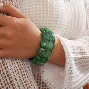 Detail shot of chunky bright green glitter resin bracelet on model wrist with knitwear