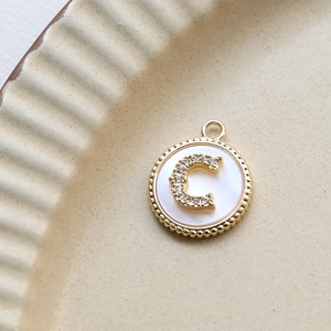 Macro view of gold-plated letter C pendant with sparkling zircons and white shell