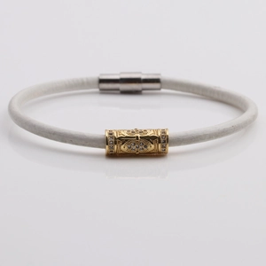 Macro detail of white braided leather bracelet with gold hollow cylinder and magnetic clasp