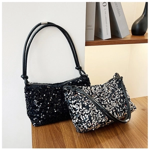 Detailed view of sequined crescent shoulder bags in black and silver on a wooden table