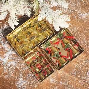 Golden Christmas bell ornaments in various sizes with red ribbons on a rustic wood background