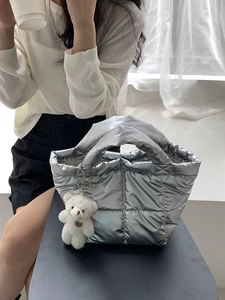 Silver quilted puffer handbag with plush teddy bear charm in a stylish casual setting