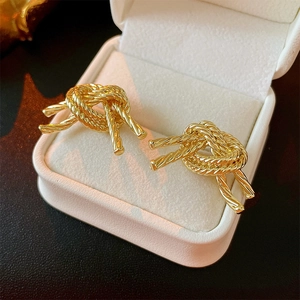 Golden knotted metallic stud earrings with brushed texture displayed in jewelry box