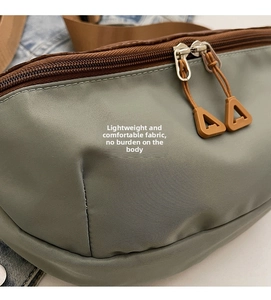Detail of sage green nylon chest bag with brown zipper trim and smooth dual metal pullers