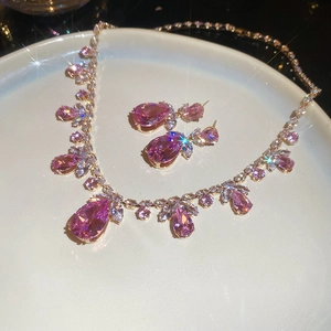 Détail macro de parure bijoux avec goutte en zircon rose et collier plaqué or chic