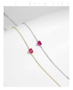Close-up of gold and silver heart-shaped bracelets with red rubies on white background