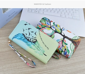 Detail view of long zip wallets with mint feather and tree of life patterns on wood
