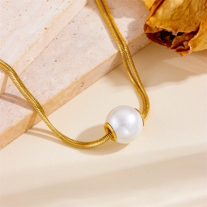 Double-layered gold snake chain necklace with large white pearl pendant on stone background