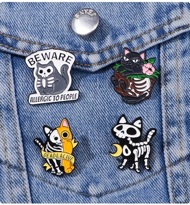 Detail of four Halloween enamel cat and skull pins on blue denim fabric background
