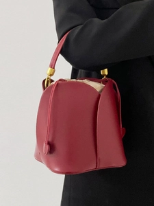 Detailed view of red petal-shaped bucket bag on arm with elegant gold hardware accents