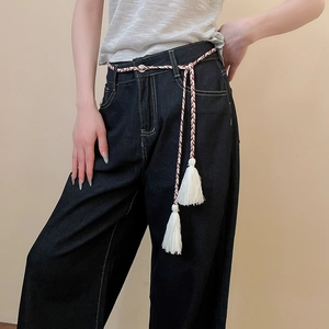 Close-up of woven rope belt with tassels on dark indigo wide-leg denim jeans