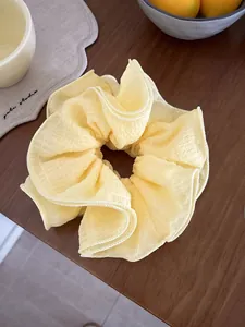 Detailed view of large light yellow ruffled scrunchie on a dark wooden tabletop