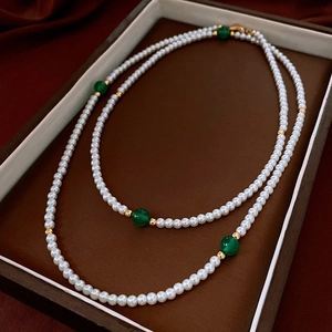 Detail of double-layer pearl necklace with green agate and gold beads on velvet tray