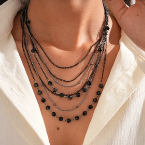 Detail of layered black beaded necklace and metal chains on white shirt model