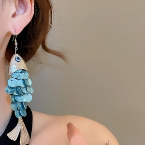 Detail of fish-shaped shell tassel earring worn by model for elegant summer beach style
