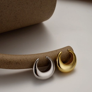 Macro shot of minimalist crescent-shaped silver and gold hoop earrings on ceramic