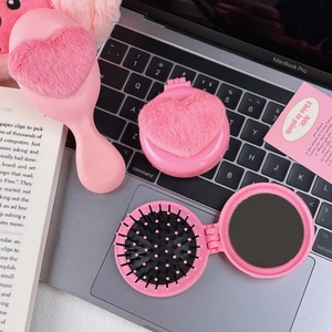 Pink plush heart hairbrush and portable folding mirror set on laptop and book