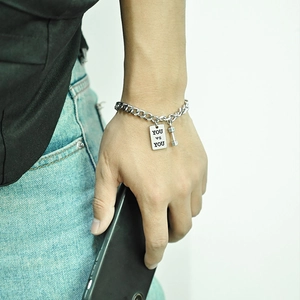 Macro detail of silver chain bracelet with dumbbell pendant and YOU vs YOU engraved tag