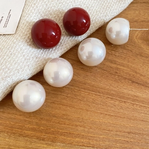 Close-up of deep red and pearlescent white round stud earrings on a beige woven fabric