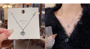Detail of silver heart planet pendant necklace with blue gemstone and cross charm on model