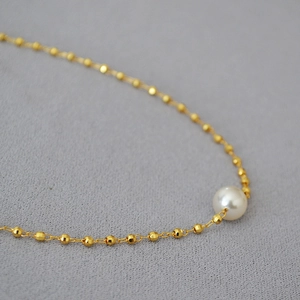 Macro shot of minimalist gold beaded chain with elegant white pearl detail