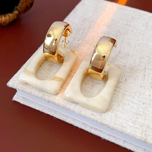 Detail of gold C-shaped earrings with beige marble resin charms on a book cover