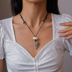 Macro detail of silver grape pendant necklace with cream bead on adjustable black wax cord