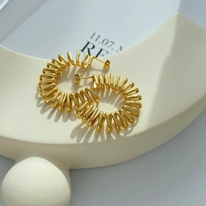Golden spring-style C-shaped hoop earrings with a metallic spiral design on a stand