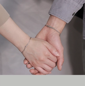 Close-up of minimalist sterling silver couple bracelets on hands with soft warm lighting