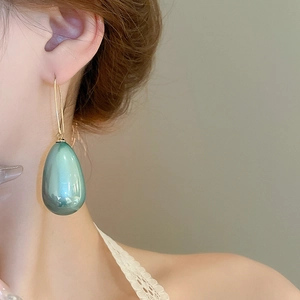 Dettaglio di grandi orecchini a goccia color verde acqua indossati da una modella