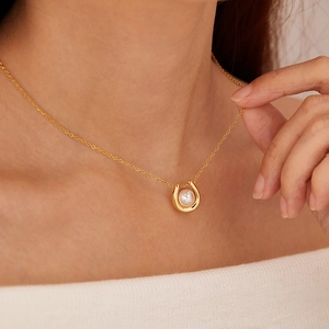 Close-up of a gold U-shaped necklace with a white pearl on a model's neck