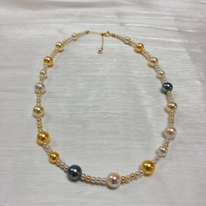Close-up of mixed color Akoya style pearl necklace on white silk fabric with golden clasp