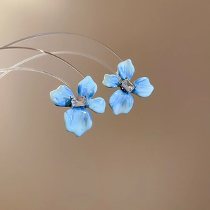 Gros plan sur les boucles d'oreilles fleurs en émail bleu clair avec gemme rectangulaire
