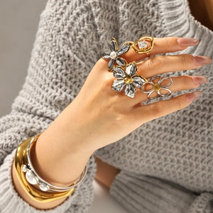 Floral zircon ring set and metallic pearl bracelet worn on grey knit sweater background