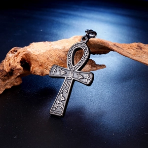 Macro detail of black metal Ankh cross pendant with ancient Egyptian hieroglyphs on wood