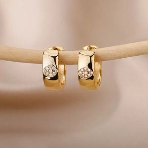 Macro shot of gold huggie earrings featuring micro-pave zircon evil eye charms on wood