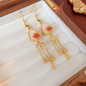 Detailed close-up of vintage tassel earrings with lotus enamel and white gemstone in a box