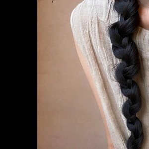 Detailed close-up showing the matte black fiber texture of the braided hair extension piece