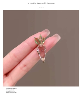 Close-up of a pink quartz carrot-shaped brooch held by fingers against a soft background