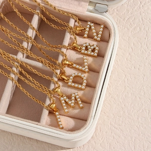 Detail of 18K gold-plated twist chains with pearl initial pendants in a jewelry box