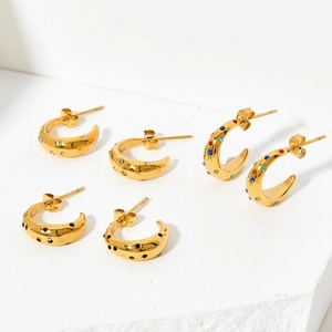 Gold C-shaped hoop earrings with colorful zircon stones on white geometric background