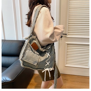 Detail of washed denim crossbody bag featuring frayed edges and white lace-up side straps
