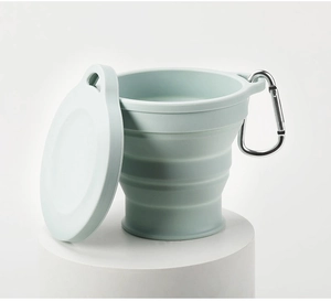 Collapsible light green silicone travel cup with lid and metal carabiner on a pedestal