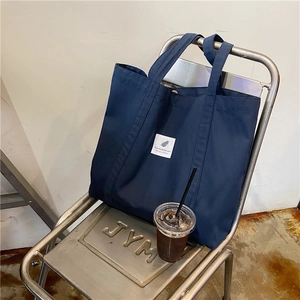 Detail of dark blue canvas tote bag on metal chair with white text label and coffee
