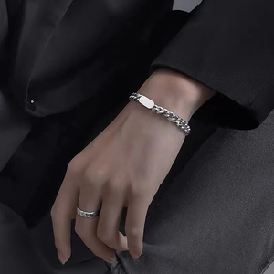 Polished silver cuban link bracelet and metal ring shown against black suit fabric