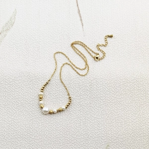 Detailed shot of a gold-plated stainless steel necklace with white pearls on white fabric