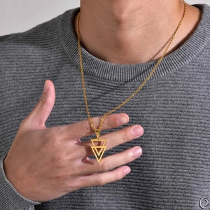 Close-up of a gold geometric triangle pendant necklace worn by a model on a grey sweater