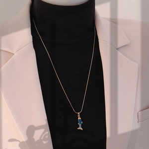 Détail d'un pendentif carpe koi vintage sur collier en acier titane doré sur un pull