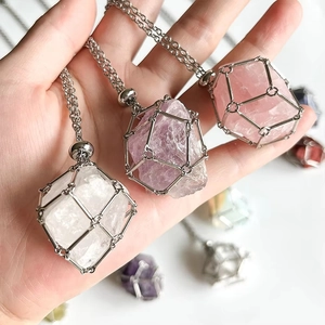 Pendentifs en cristal naturel brut dans des cages en métal doré présentés à la main sur blanc