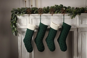 Close-up of four dark green knitted Christmas stockings with scales hanging on fireplace